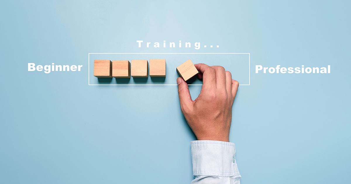 Hand placing the final wooden block in a row between the words &ldquo;Beginner&rdquo; and &ldquo;Professional,&rdquo; illustrating the journey from beginner to professional through training.
